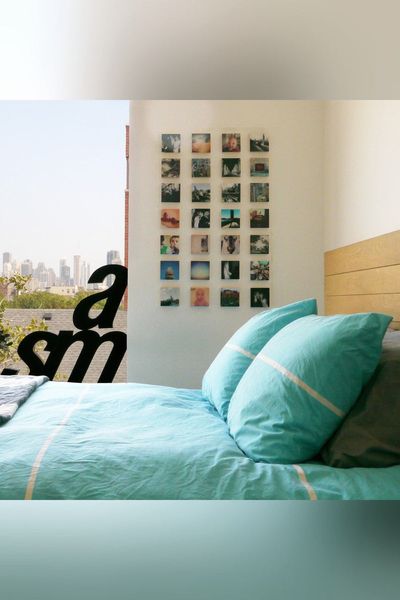 A four by five grid of twenty small wood photo blocks on a bedroom wall beside a bed
